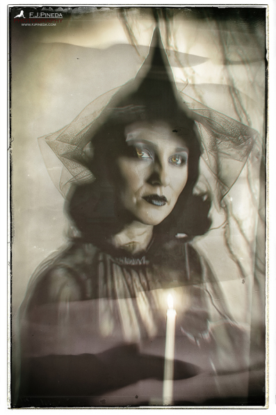 Retrato de una bruja con sombrero y velo oscuro junto a una vela encendida, en una imagen íntima y misteriosa.
