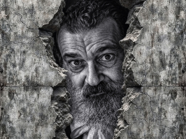 Hombre barbado asomando desde una abertura en un muro agrietado, en una imagen oscura de la serie La Grieta de F. J. Pineda.