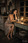 Chloe sentada ante una mesa con objetos iluminados por una luz cálida, en una escena interior de Las Habitaciones de Chloe.