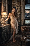 Chloe de pie junto a la puerta de una habitación antigua, con vestido claro y luz cálida, serie Las Habitaciones de Chloe de F. J. Pineda.