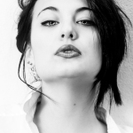 Retrato en blanco y negro de una mujer adulta con camisa blanca, mirada directa y cabello oscuro sobre fondo claro.