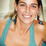 Retrato luminoso de una mujer adulta sonriente con top turquesa y pendientes azules.
