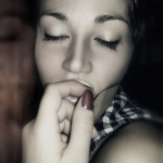 Retrato íntimo de mujer adulta con los ojos cerrados, una mano junto a la boca y un tatuaje visible en la muñeca.