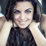 Retrato de mujer adulta sonriente con el rostro apoyado entre las manos y larga melena oscura.