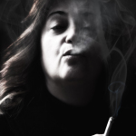 Retrato en blanco y negro de mujer adulta fumando, con el humo cubriendo parcialmente el rostro.