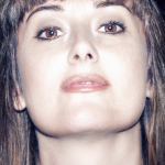 Retrato cercano de mujer adulta tomado desde un ángulo bajo, con flequillo y mirada frontal.