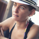 Retrato de mujer adulta con sombrero blanco de ala corta, brazos cruzados y mirada clara hacia un lado.