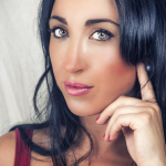 Retrato de mujer adulta con cabello negro, top rojo y una mano apoyada junto a la mejilla.