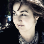 Retrato exterior de mujer adulta con el pelo movido por el viento y varios collares metálicos.