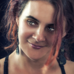 Retrato de mujer adulta con cabello oscuro y mechones rojizos, mirando a cámara con media sonrisa.
