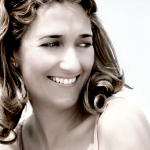 Retrato luminoso de mujer adulta sonriendo al aire libre, con el cabello ondulado y luz suave.
