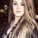 Retrato nocturno de mujer adulta con larga melena clara, chaqueta oscura y fondo desenfocado.