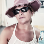 Retrato de mujer adulta con sombrero rosa de ala ancha, gafas de sol negras y vestido blanco.