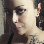 Retrato cercano de mujer adulta con piercing en la nariz, tatuaje en el hombro y media luz sobre el rostro.