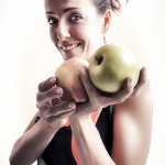 Retrato de mujer adulta sonriendo mientras sostiene dos manzanas grandes entre las manos.