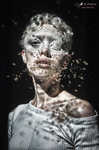 Retrato de una figura con el rostro parcialmente cubierto por pequeñas polillas o fragmentos orgánicos, con un ojo cerrado y luz dramática sobre fondo negro.