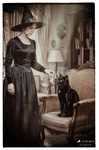 Bruja vestida de negro en una habitación antigua, acompañada por un gato negro, dentro de la galería Brujas de F. J. Pineda.
