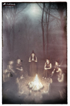 Escena nocturna en un bosque oscuro con varias luces o velas encendidas alrededor de una figura central, evocando un ritual de brujas.