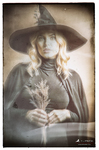 Retrato de una bruja rubia con sombrero negro sosteniendo un ramo de hierbas secas entre las manos.