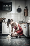 Mujer adulta con delantal rojo arrodillada en el suelo de una cocina, limpiando un derrame junto a un cuenco.