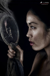 Retrato de perfil de una mujer sosteniendo un pequeño espejo de mano, con expresión concentrada y fondo oscuro.