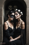 Dos mujeres adultas vestidas de negro, con rostros pálidos o máscaras blancas, posando juntas en una escena oscura y teatral.