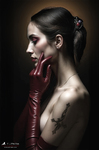 Mujer adulta de perfil con largo guante rojo junto al rostro, sobre fondo oscuro y luz lateral.