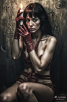 Mujer adulta sentada con dedos pintados de rojo cerca del rostro, en una composición oscura de gesto intenso.