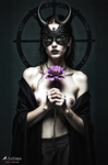 Mujer adulta con máscara negra de cuernos, sosteniendo una flor morada ante el pecho en una composición ritual.