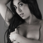 Retrato íntimo de mujer adulta con cabello oscuro, sosteniendo una prenda junto al pecho.