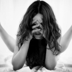 Mujer adulta sentada con el rostro cubierto parcialmente por el cabello y una mano apoyada en la cabeza.