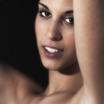 Primer plano de mujer adulta sonriendo ligeramente, con un brazo elevado y fondo oscuro.