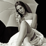 Mujer adulta sentada con una sombrilla blanca y vestido claro, en una escena luminosa y delicada.