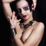 Retrato de mujer adulta con maquillaje artístico oscuro y mano levantada junto al rostro.