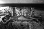 Mujer adulta desnuda recostada en un sofá antiguo, con un brazo elevado hacia la cabeza y luz suave.