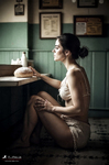 Mujer adulta sentada de perfil junto a una ventana, sosteniendo una bandeja con un pan en una cocina de aire antiguo.