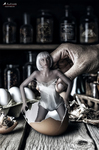 Mujer adulta sentada junto a una pequeña figura blanca, en un interior oscuro con botellas y objetos de laboratorio al fondo.