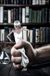 Pequeña figura femenina sentada o apoyada sobre una gran mano humana, con libros al fondo en una escena de escala imposible.