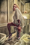 Mujer adulta sentada en un baño antiguo y desordenado, con botas altas rojas y luz cálida de interior.