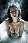 Mujer adulta en una bañera llena de vapor, con el rostro húmedo y expresión intensa hacia la cámara.