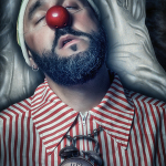 Retrato de un hombre barbado tumbado con nariz roja de payaso y camisa de rayas, iluminado con luz fría.