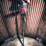 Figura de payaso subida a un alto soporte dentro de una estructura circular con paredes de rayas.