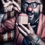 Hombre con gafas y expresión exagerada sosteniendo una caja pequeña, en una escena de humor oscuro y teatral.