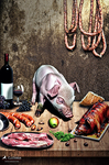 Bodegón de mesa con una cabeza de cerdo o pieza de carne, embutidos colgados, vino, verduras y alimentos dispuestos de forma abundante.
