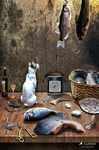 Bodegón con varios peces sobre una mesa, acompañado por botellas, una cesta y pequeños objetos de cocina en un ambiente sobrio.