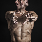 Hombre adulto desnudo extendiendo ambos brazos hacia delante, en una pose frontal de gran intensidad.