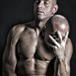 Hombre adulto desnudo sosteniendo una calavera junto al hombro, en una imagen oscura de aire meditativo.