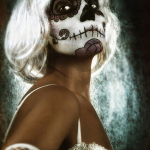 Retrato de mujer adulta con peluca blanca y maquillaje de calavera, girando el rostro sobre fondo oscuro.