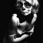 Retrato en blanco y negro de mujer adulta con maquillaje de calavera, inclinada hacia la cámara con expresión intensa.