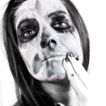 Primer plano de mujer adulta con maquillaje de calavera, sin peluca, tocándose los labios en una imagen intensa y cercana.